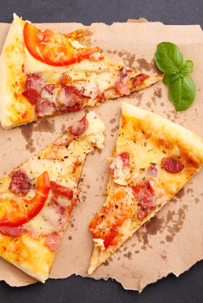 Pizza aux saucisses, jambon, tomates et fromage, décorée au basilic et coupée en morceaux sur un parchemin