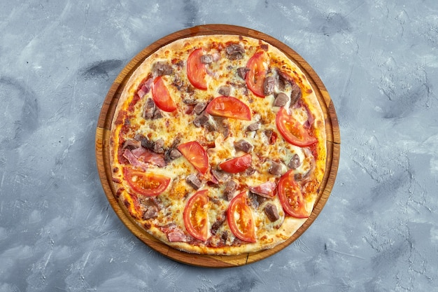 Pizza aux tomates, bacon, boeuf et fromage sur fond gris