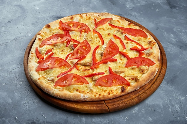 Pizza aux tomates, poivrons, poulet et fromage sur un plateau en bois