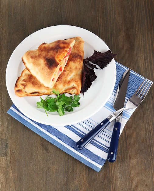 Photo pizza calzone sur une assiette sur une serviette sur une table en bois