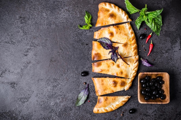 La pizza calzone fermée est coupée en morceaux sur un tableau noir