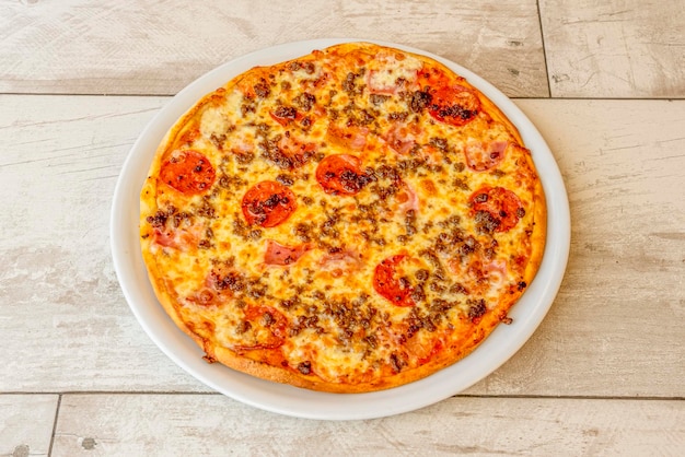 Pizza cannibale avec bacon, boeuf haché, tranches de pepperoni et beaucoup de fromage mozzarella sur une assiette ronde en porcelaine blanche