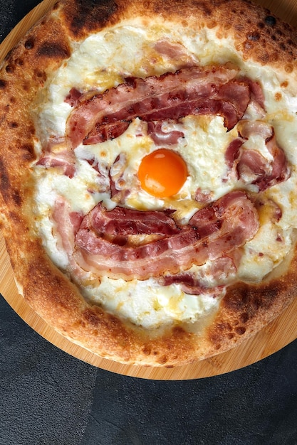 Pizza carbonara avec bacon et œuf sur fond de pierre sombre
