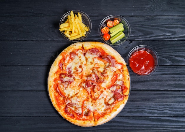 Pizza chaude fraîche avec frites et légumes sur fond sombre