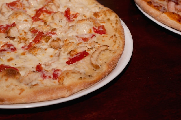 Pizza avec une croûte dorée, du poivron et du fromage sur une plaque blanche sur une table en bois