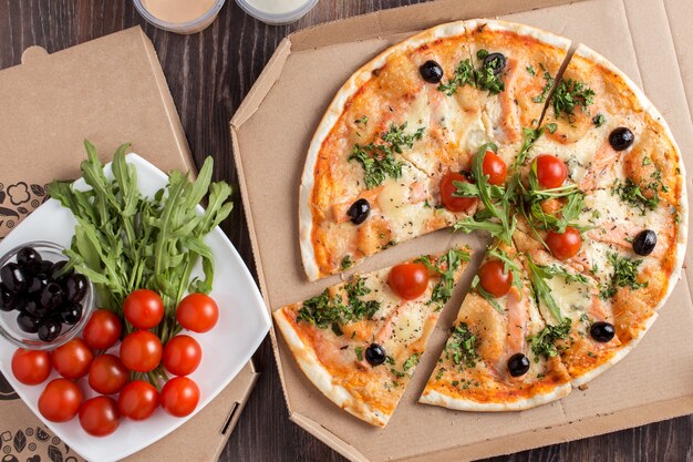 Pizza à croûte mince en tranches avec du saumon dans une boîte en carton