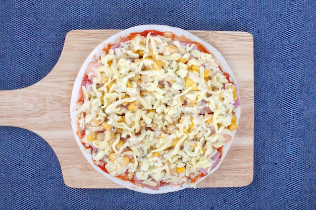 Pizza crue sur planche de bois sur une nappe bleue avec vue de dessus