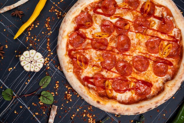 Photo pizza épicée avec des saucisses et des piments sur un fond de pierre noire espace libre pour le texte