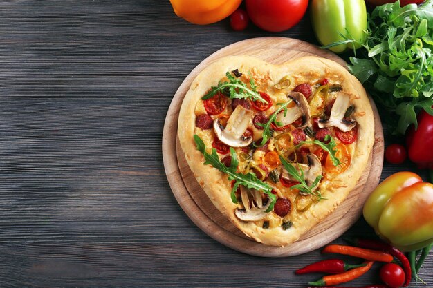 Pizza en forme de coeur et légumes frais sur fond de bois