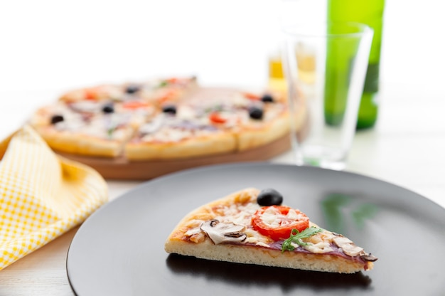 Pizza fraîche dans un style italien rustique avec des champignons d'olives séchées et trois sortes de fromage sur un fond en bois clair avec une bouteille de bière froide