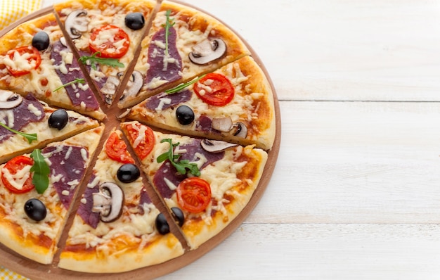 Pizza fraîche dans un style italien rustique avec des champignons d'olives séchées et trois sortes de fromage sur un fond en bois clair