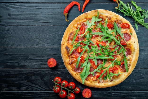 Pizza fraîche faite maison avec salami, tomates cerises pepperoni et roquette sur un bois noir avec copie espace.