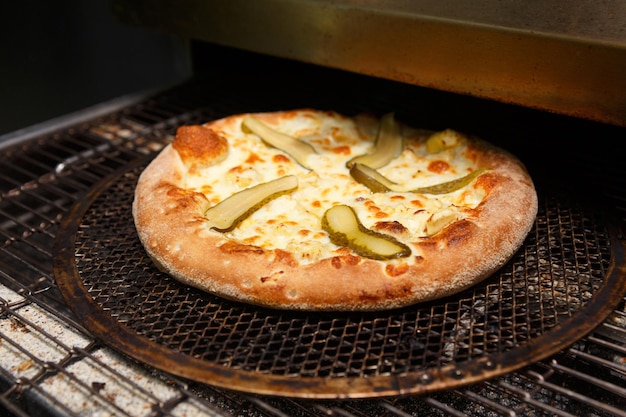 Une pizza fraîchement cuite avec des concombres et de la mozzarella sort d'un four à convoyeur moderne dans un restaurant