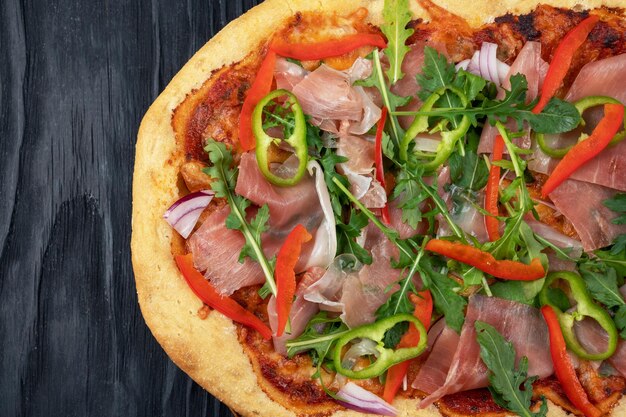 Pizza italienne sur assiette avec tranches de jamon poivre et feuilles de roquette fraîches sur le dessus