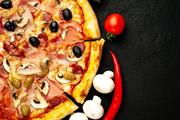 pizza italienne avec bacon, champignons, olives, tomates sur un fond de béton noir avec copie espace pour votre texte