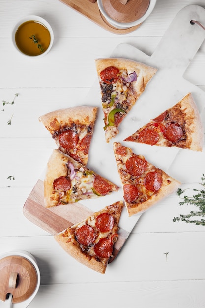 Pizza italienne chaude avec tomates fondantes, pepperoni et fromage sur une table en bois rustique blanche.