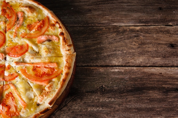 Pizza italienne délicieuse fraîchement cuite au four servie sur une table rustique en bois, mise à plat. Fond sombre avec espace libre pour le texte. La cuisine traditionnelle.