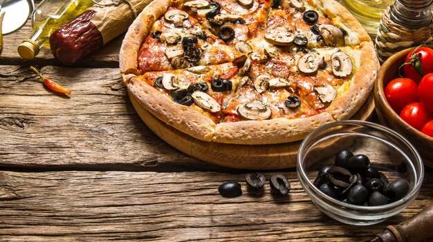 Photo pizza italienne et différents ingrédients - viande, champignons, tomates et huile d'olive sur fond de bois