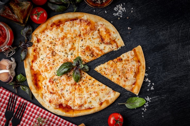 Pizza italienne Margarita coupée en morceaux et ingrédients pour sa préparation sur la vue de dessus de table