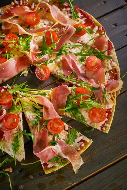 Pizza italienne avec salami, tomates, fromage et herbes sur table en bois vintage. Vue de dessus