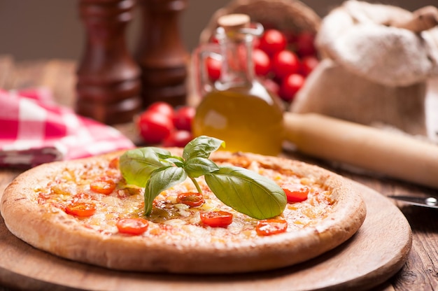 Pizza italienne à la tomate garnie de fromage doré fondu, d'herbes et de basilic servi sur une planche de bois ronde sur une vieille table en bois