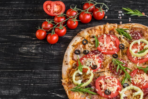 Pizza de légumes, champignons et tomates sur fond noir en bois. Il peut être utilisé comme arrière-plan