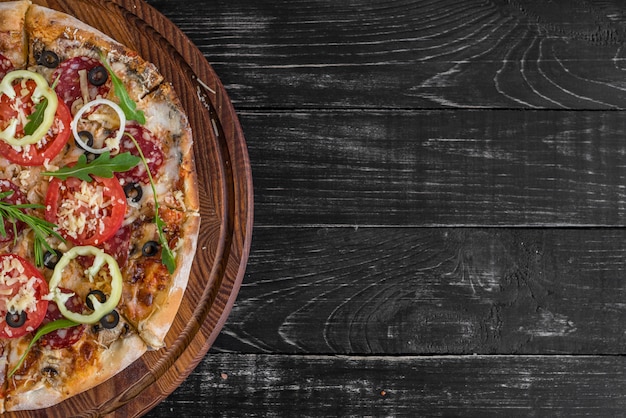 Pizza de légumes, champignons et tomates sur fond noir en bois.