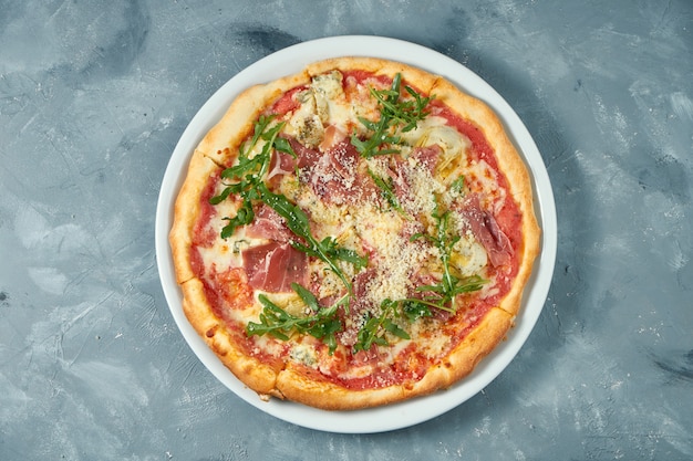 Pizza maison au jambon, roquette et parmesan dans une assiette blanche sur une surface en béton. Fermer. Mise au point sélective