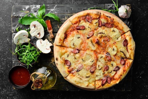 Pizza maison aux saucisses, champignons et fromage Sur fond de pierre noire Espace libre pour le texte