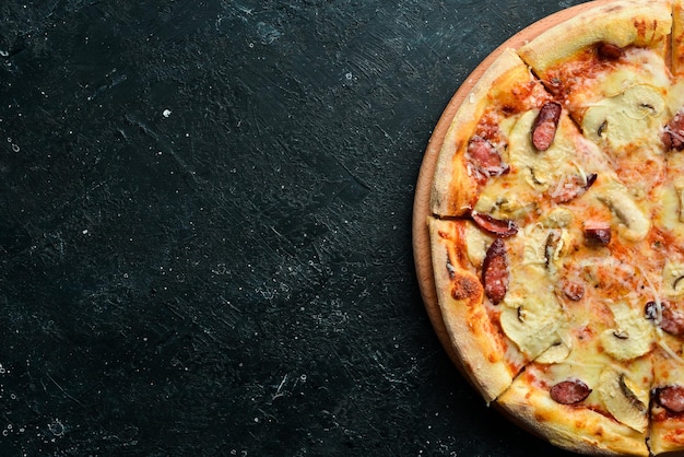Pizza maison aux saucisses, champignons et fromage Sur fond de pierre noire Espace libre pour le texte