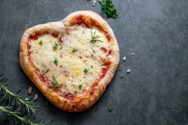 Pizza maison en forme de coeur avec pâte au levain et fromage pour la Saint-Valentin sur fond sombre. Espace de copie vue de dessus