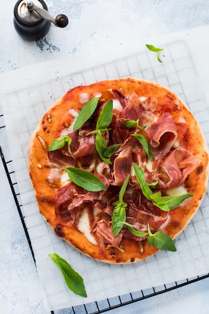 Pizza maison avec jambon, mozzarella et feuilles de basilic sur fond de béton ancien. Vue de dessus.