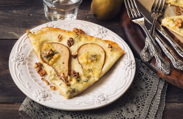 Pizza maison avec poire, fromage bleu, mozzarella et noix sur une surface en bois rustique.