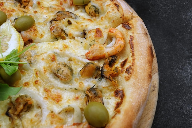 Pizza marinara aux moules de calamars crevettes olives et citron sur une planche ronde en bois sur la vue de dessus en béton gris