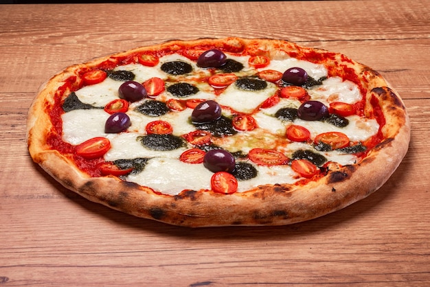 Pizza à la mozzarella de bufflonne avec tomates cerises au pesto de basilic et olives noires sur une table en bois rustique