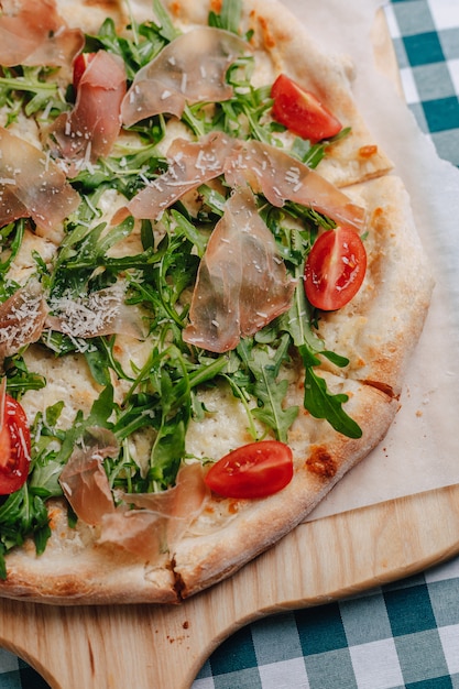 Pizza napolitaine avec salami, roquette, tomates saupoudrées de fromage sur une planche de bois sur une nappe dans une cellule avec une place pour le texte