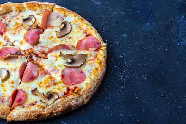 Une pizza préparée avec des champignons, du jambon et du fromage sur un fond sombre. Déjeuner ou dîner traditionnel italien. Concept de restauration rapide et de cuisine de rue. À plat, vue de dessus, espace de copie pour le texte