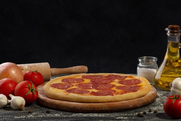 Pizza prête au salami sur une planche de bois et fond noir Fond culinaire