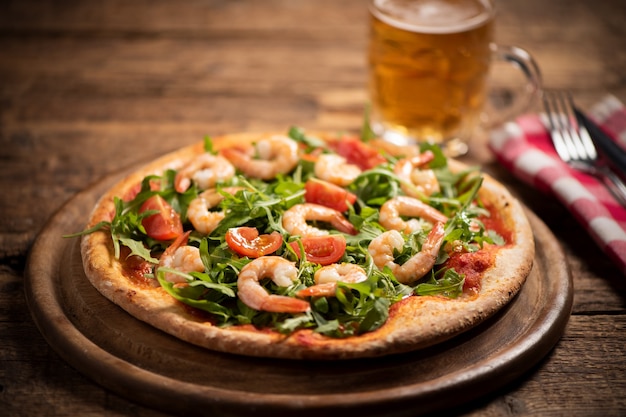 Pizza recouverte de roquette et crevettes sur table en bois close up