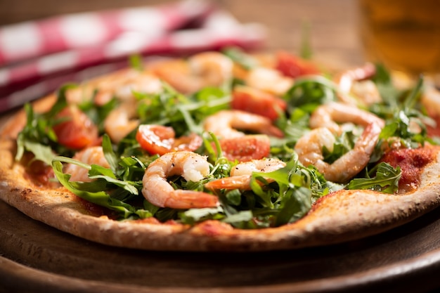 Pizza recouverte de roquette et crevettes sur table en bois close up