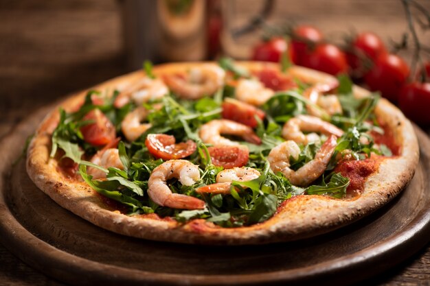 Pizza recouverte de roquette et crevettes sur table en bois close up