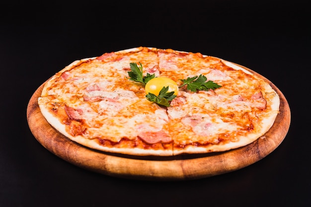 Pizza ronde avec un oeuf sur une planche en bois sur fond noir