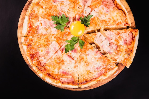 Pizza ronde avec un oeuf sur une planche en bois sur fond noir