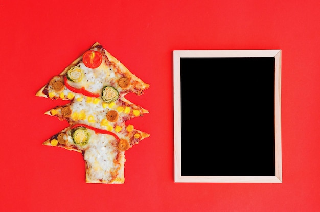 Pizza sapin de Noël avec tomates, légumes et fromage sur fond rouge. Nourriture créative et amusante