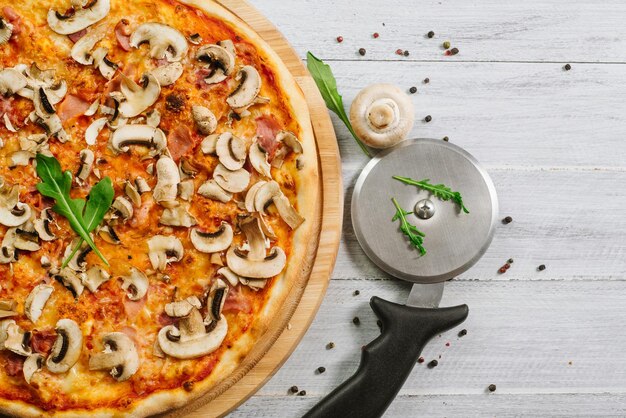 Pizza savoureuse Caprizzioza avec sauce tomate, jambon et champignons sur le fond en bois blanc