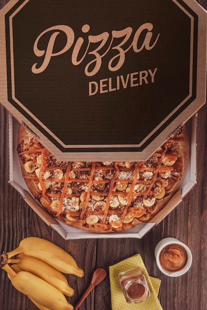 Photo pizza sucrée brésilienne avec banane, dulce de leche et cannelle dans une boîte de livraison - vue de dessus.