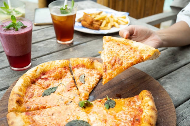 Une pizza sur la table prise un morceau avec les mains et le jus frais