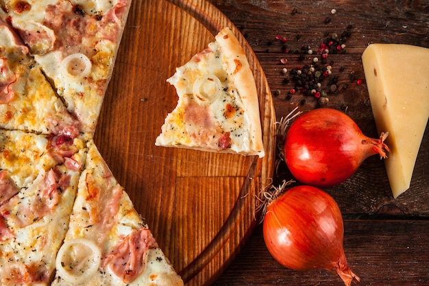 Pizza en tranches avec morceau de morsure, servie sur une table en bois avec oignon, fromage et poivre