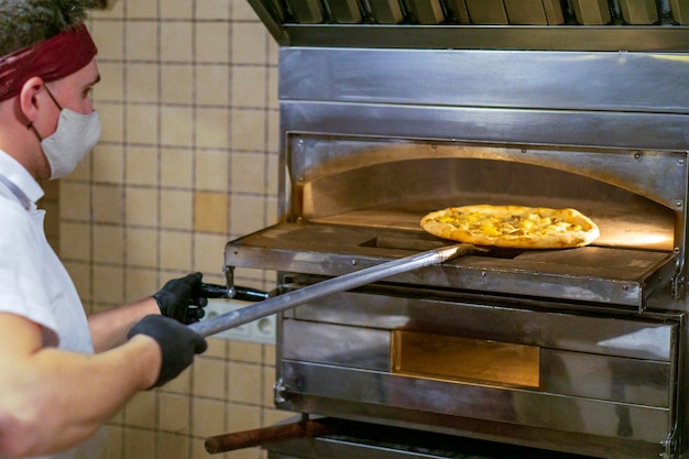 Un pizzaiolo masqué sort la pizza dans un four chaud