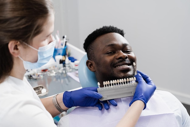 Placages ou implants échantillons de couleur des dents pour le blanchiment des dents pour un patient africain dans une clinique dentaire Guide des nuances de couleur des dents gros plan Homme africain en dentisterie